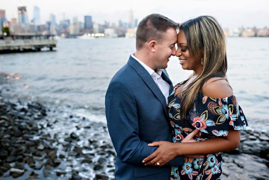 A sexy couple stand on the rocks along the hudson river in hoboken, NJ for their engagement Session.